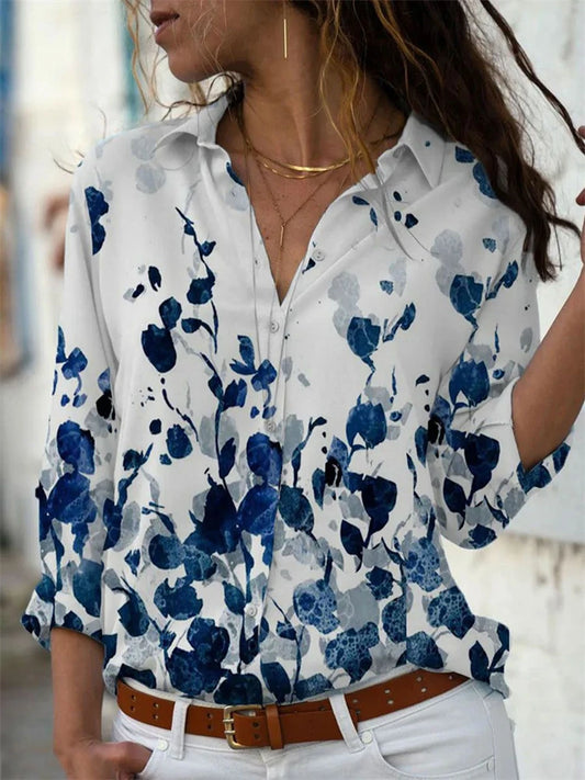 Woman wearing a white shirt with blue floral pattern, standing outdoors.