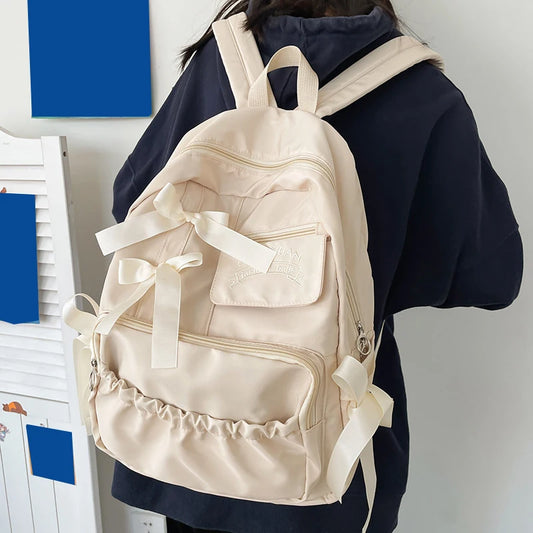 Beige backpack with ribbons worn by a person against a white background