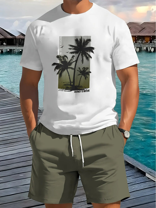 Person wearing a white t-shirt with palm tree design and green shorts by a waterfront.