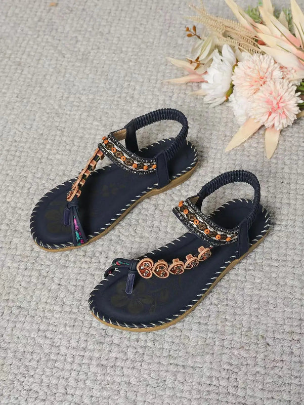 Navy sandals with decorative straps on a textured surface with flowers.