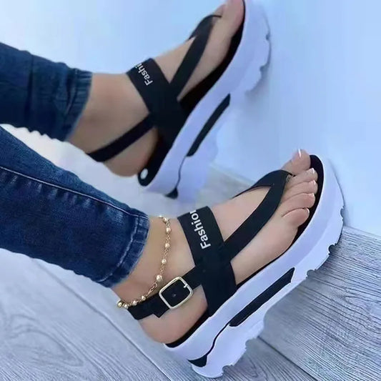 Black sandals with white soles worn by a person on a light blue background