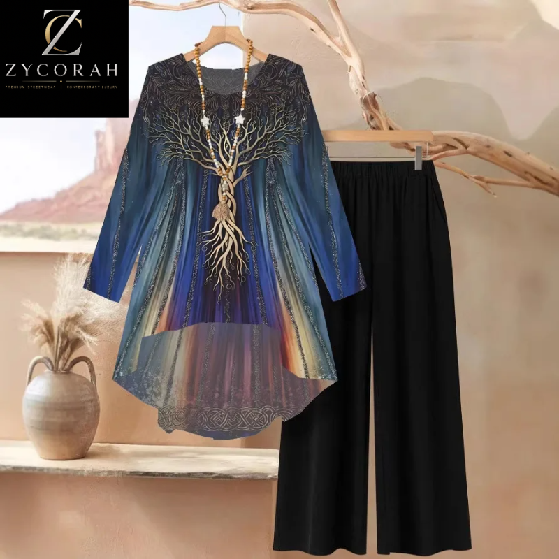 A women's two-piece outfit set featuring a long-sleeve high-low tunic top with a blue and gold tree of life print, paired with solid black wide-leg pants. The set is displayed on a hanger and a wooden stand against a warm, neutral background with a decorative vase.