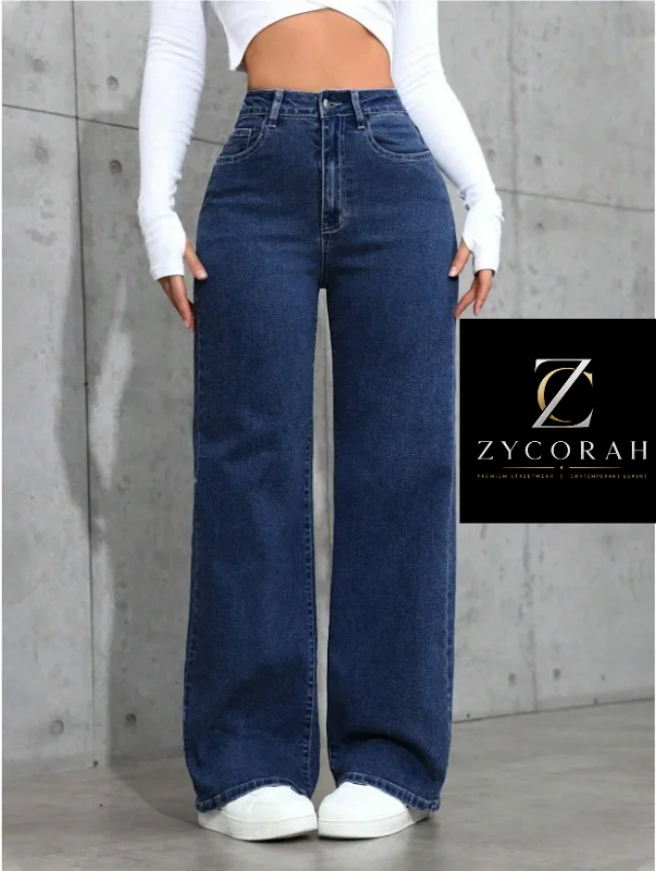 A model wearing high-waisted, wide-leg dark blue denim jeans with a white long-sleeve crop top and white sneakers, standing against a concrete wall. A black brand overlay for 'Zycorah' is visible on the right side.