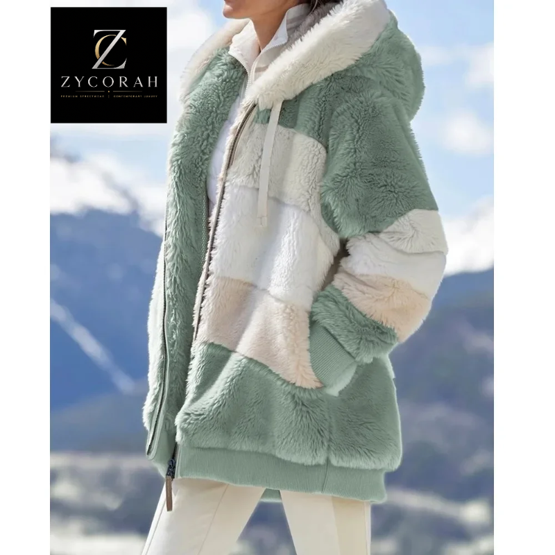 A woman wearing a soft sherpa fleece zip-up jacket with large color-blocked panels in sage green, cream, and off-white, photographed outdoors against a blurred mountain landscape. A ZYCORAH brand logo appears in the top-left corner.