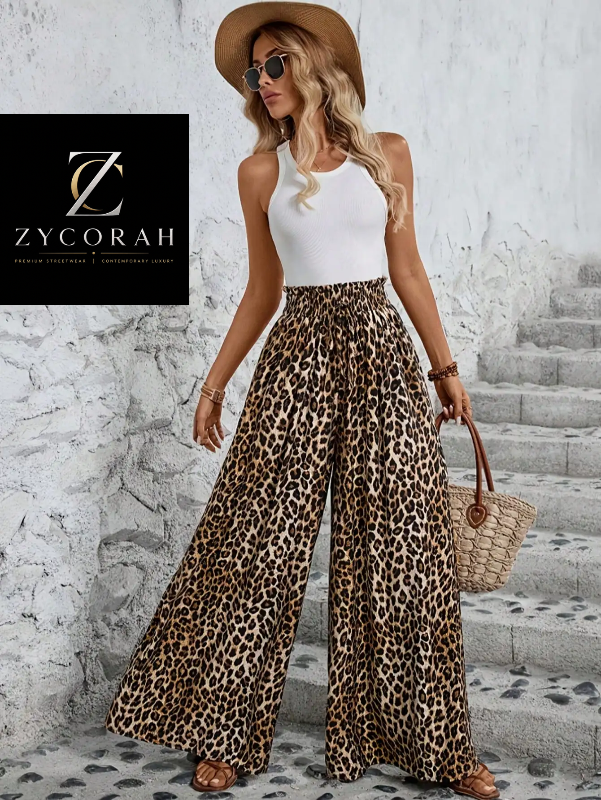 A woman models a white ribbed tank top and high-waisted leopard-print wide-leg pants, styled with a tan wide-brim hat, sunglasses, bracelets, and a woven straw handbag. She stands on stone steps against a textured white wall, with a Zycorah brand logo overlay in the top-left corner.