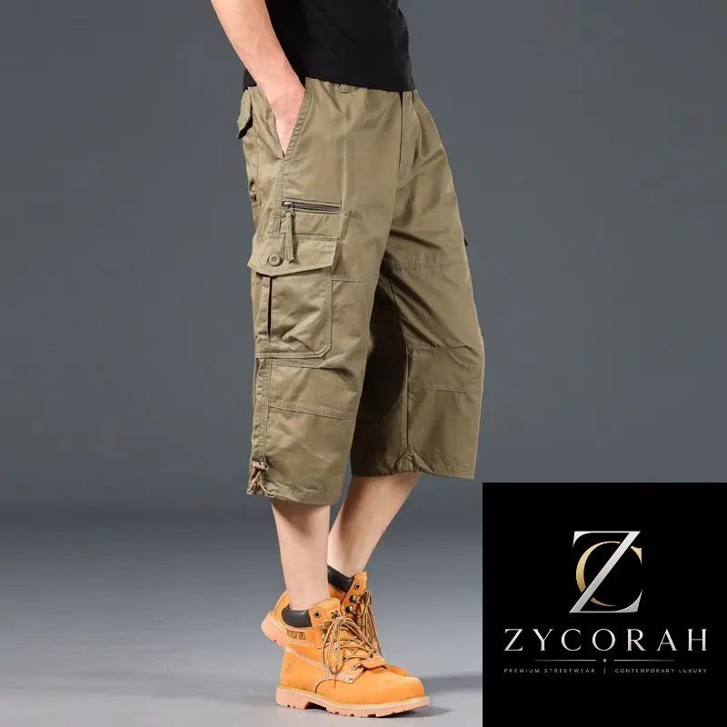 A model wearing olive green cargo shorts with side zippers and flap pockets, paired with a black shirt and orange work boots, shown against a gray studio background with a Zycorah brand logo in the bottom right corner.