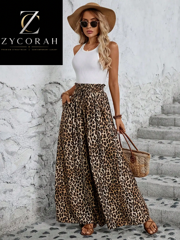 A woman models a white ribbed tank top and high-waisted leopard-print wide-leg pants, styled with a brown wide-brim hat, sunglasses, a woven straw bag, and brown sandals. She stands against a textured white wall with stone steps.
