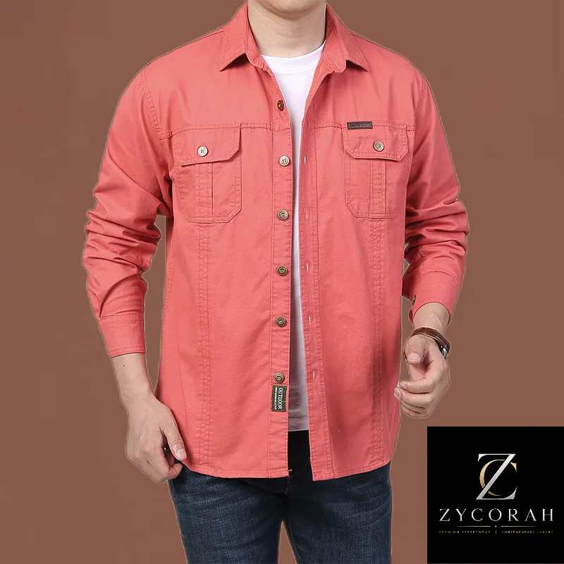 A man wearing a coral pink long-sleeve button-up shirt with two chest pockets, styled over a white t-shirt and blue jeans, against a solid brown background.