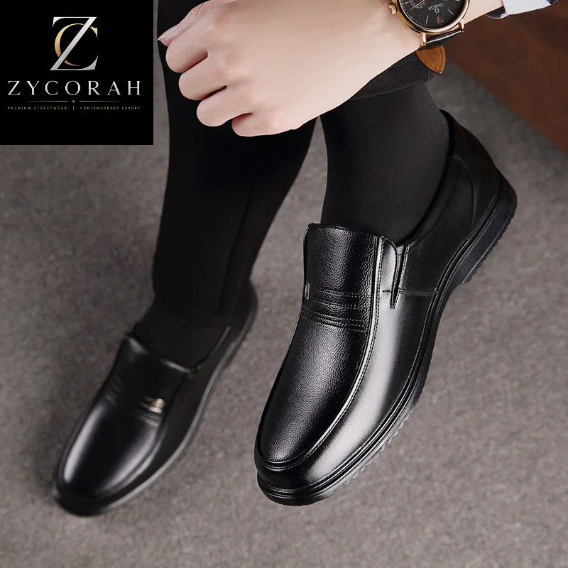 A person wearing black leather slip-on loafers with black tights, shown from the knees down on a gray carpet. A watch is visible on the wrist, and a ZYCORAH brand overlay appears in the top left corner.