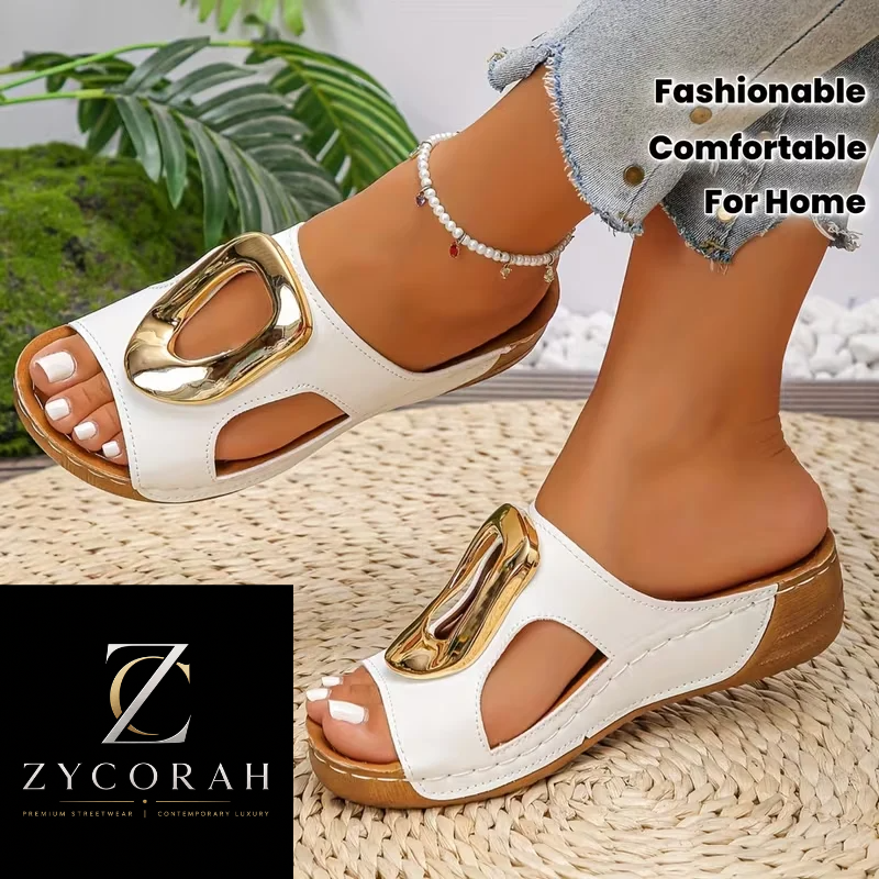 White open-toe wedge slide sandals with large gold-tone metal accents, shown on a model's feet on a woven mat. The image includes a black brand box for ZYCORAH in the lower left and text reading 'Fashionable Comfortable For Home' in the upper right.