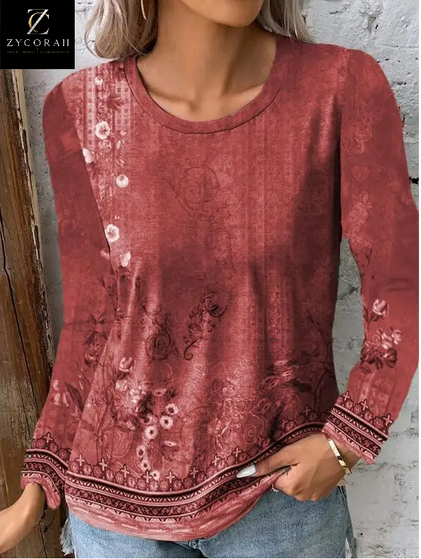 A woman wearing a long-sleeve dusty rose top with a faded floral and paisley pattern, paired with light blue jeans. The ZYCORAH brand logo is visible in the top-left corner.