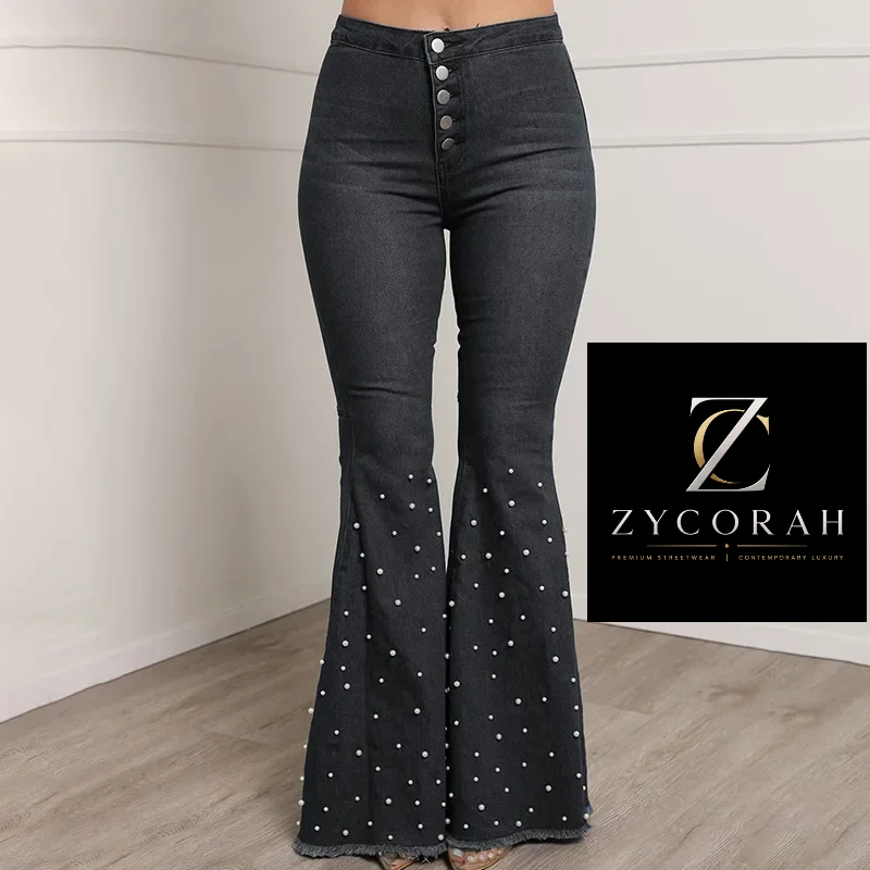 A model is wearing dark gray flare jeans with white polka dots and a button fly, standing in a room with a light-colored wall and wood floor. A black brand logo for 'Zycorah' is shown in the bottom right corner.