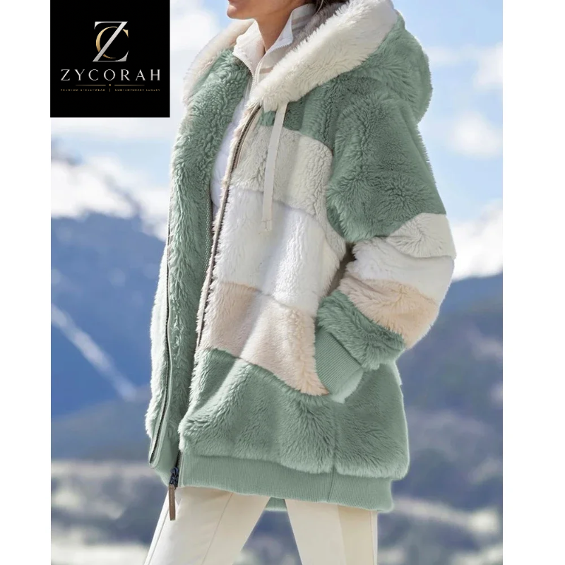 A woman wearing a soft sherpa fleece hooded jacket with large color-blocked panels in sage green, cream, and off-white, photographed outdoors against a blurred mountain landscape. A ZYCORAH logo appears in the top-left corner.