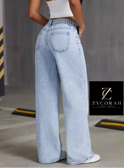 A model from the back wearing light-wash wide-leg denim jeans, a white crop top, and white sneakers in an industrial setting. A black ZYCORAH brand logo overlay is visible on the right side.