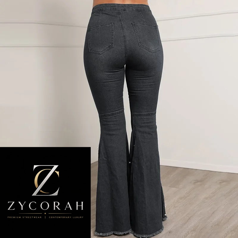 A person wearing dark charcoal gray flare jeans, shown from the back in a studio setting with a white paneled wall and light wood floor. A black brand overlay in the bottom left corner displays the Zycorah logo and name.