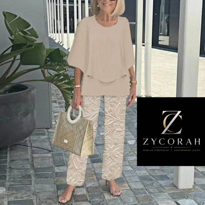 A woman models a beige two-piece outfit consisting of a short-sleeve draped top and matching patterned trousers, holding a woven beige handbag. A black brand overlay for 'Zycorah' is visible on the bottom right.
