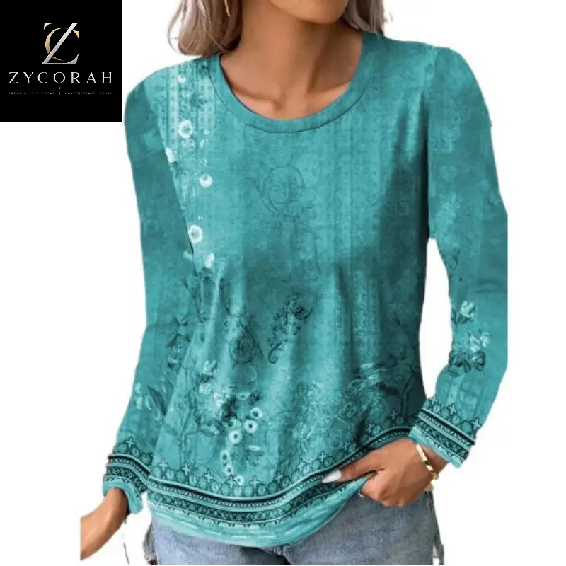 A woman wearing a teal long-sleeve tunic top with a subtle vintage floral and botanical print, featuring a decorative patterned hem and cuffs. The ZYCORAH brand logo is visible in the top-left corner.