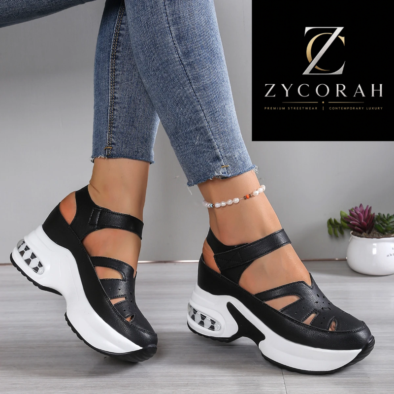A pair of black and white chunky platform sandals with cutout details, shown on a model wearing blue jeans. The background is a clean gray studio setting with a ZYCORAH logo in the top right corner.
