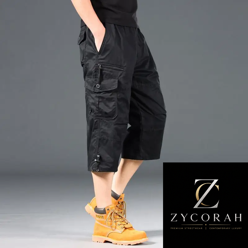 A model wearing black cargo shorts with multiple utility pockets and drawstring details, paired with yellow boots, shown from the waist down against a gray studio background. A Zycorah brand logo is displayed in the bottom right corner.