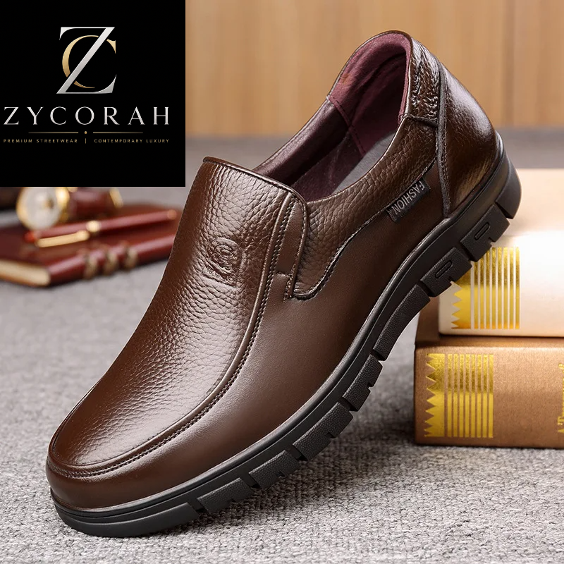 A brown textured leather slip-on loafer shown at an angle on a gray carpet, with books in the background and a ZYCORAH brand logo overlay in the top left corner.