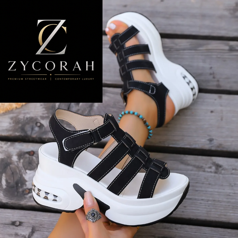 Black platform wedge sandals with multiple cutout straps and a chunky white sole, shown being worn and held in a hand against a rustic wooden deck background. A Zycorah logo panel appears in the top left.