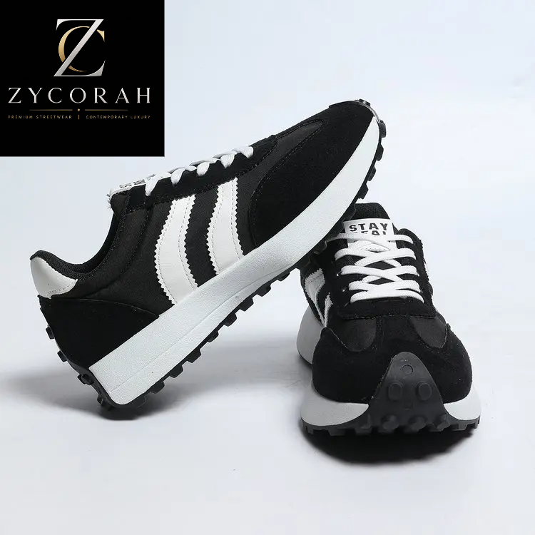 A pair of black and white low-top sneakers shown on a clean white studio background, with a black square logo in the top-left corner reading ZYCORAH.