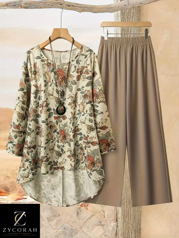 A women's two-piece outfit set featuring a long-sleeve floral tunic top in beige with rust and green botanical patterns, paired with high-waisted, wide-leg taupe pants. The garments are displayed on wooden hangers against a rustic, warm-toned background with a ZYCORAH brand logo overlay in the bottom-left corner.