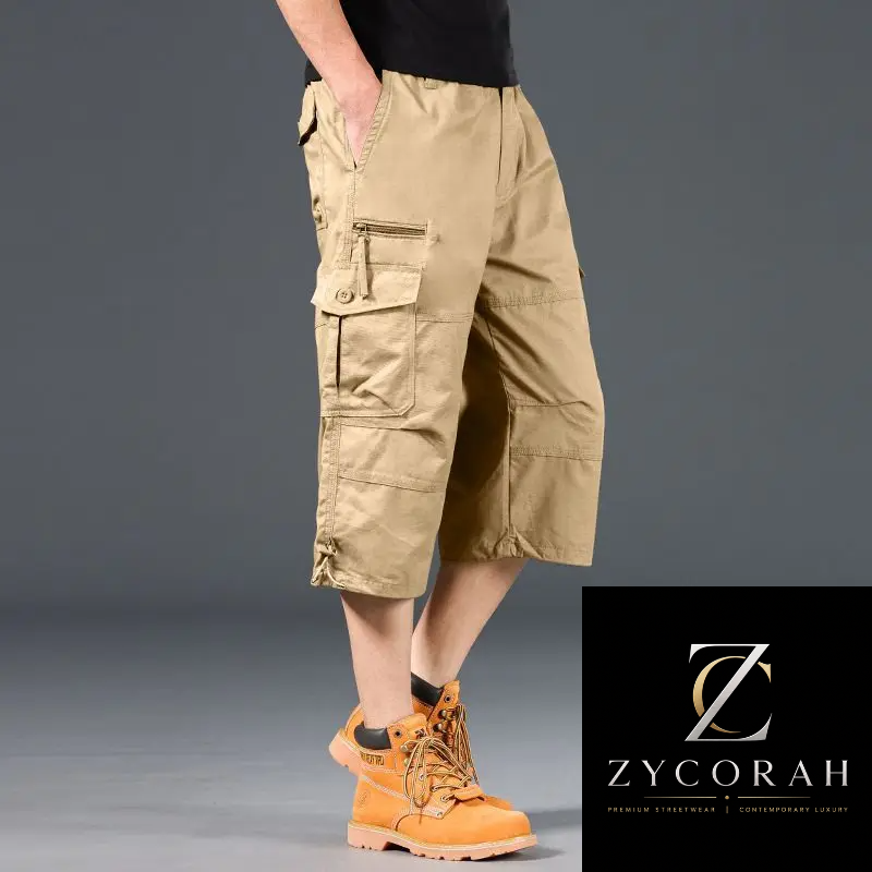 A model from the waist down wearing tan cargo shorts, a black t-shirt, and orange work boots, set against a dark gray studio background with a ZYCORAH brand logo in the bottom right corner.
