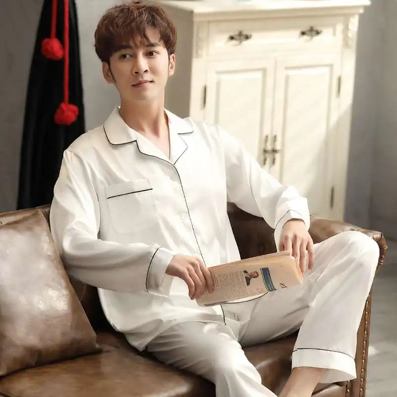 Man in white pajamas holding a book on a brown couch.