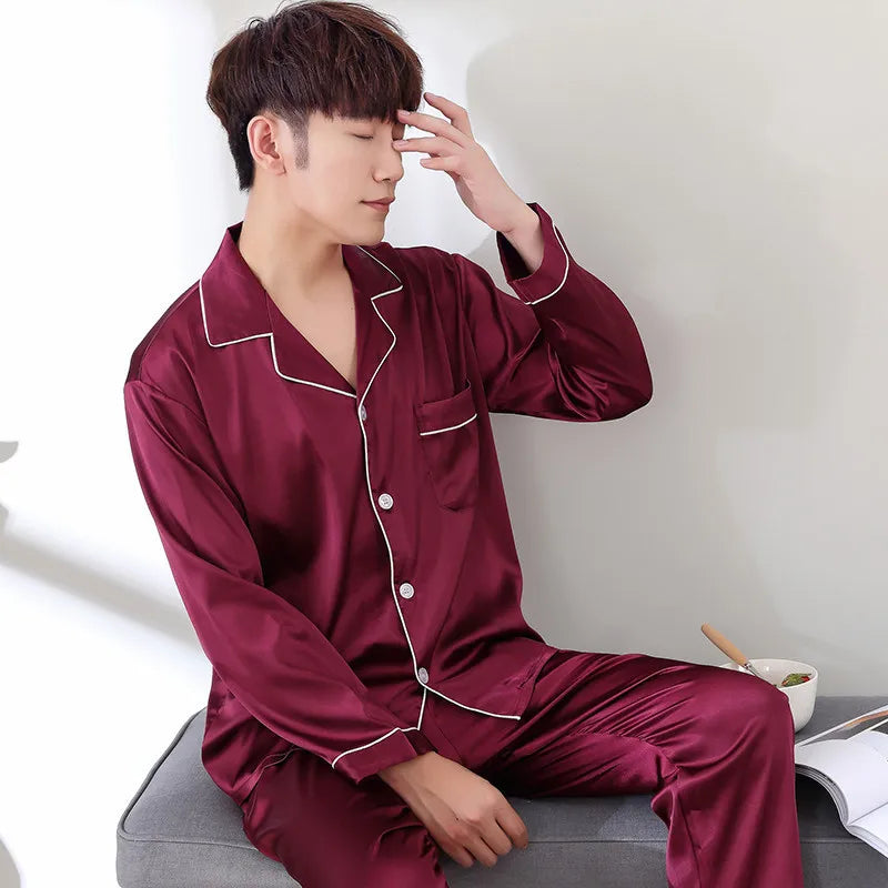Man wearing burgundy satin pajamas sitting on a couch.