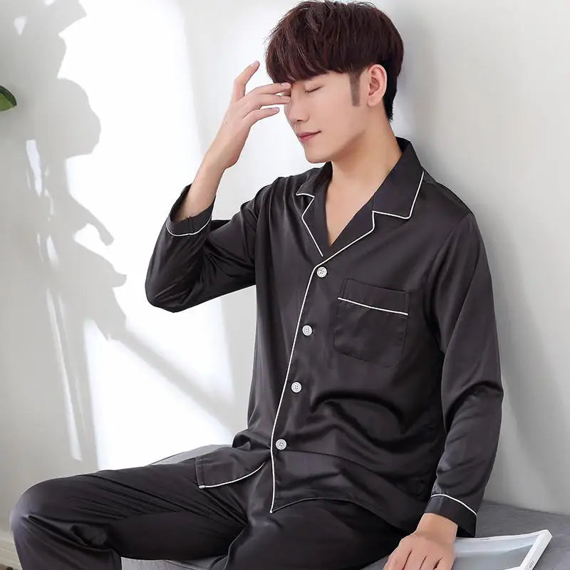 Man wearing black pajamas with white trim sitting against a white wall.