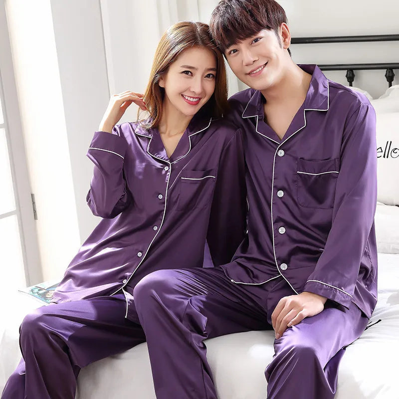 Couple wearing matching purple pajamas sitting on a bed.
