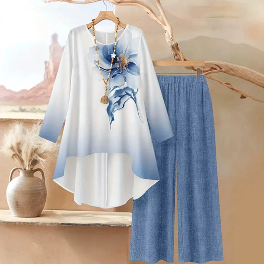 White blouse with blue floral design and blue pants on a wooden hanger against a desert landscape background.