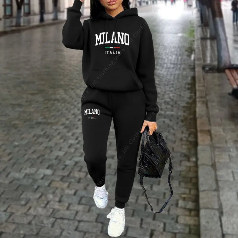 Person wearing a black 'Milano Italia' hoodie and jogger set on a city street.