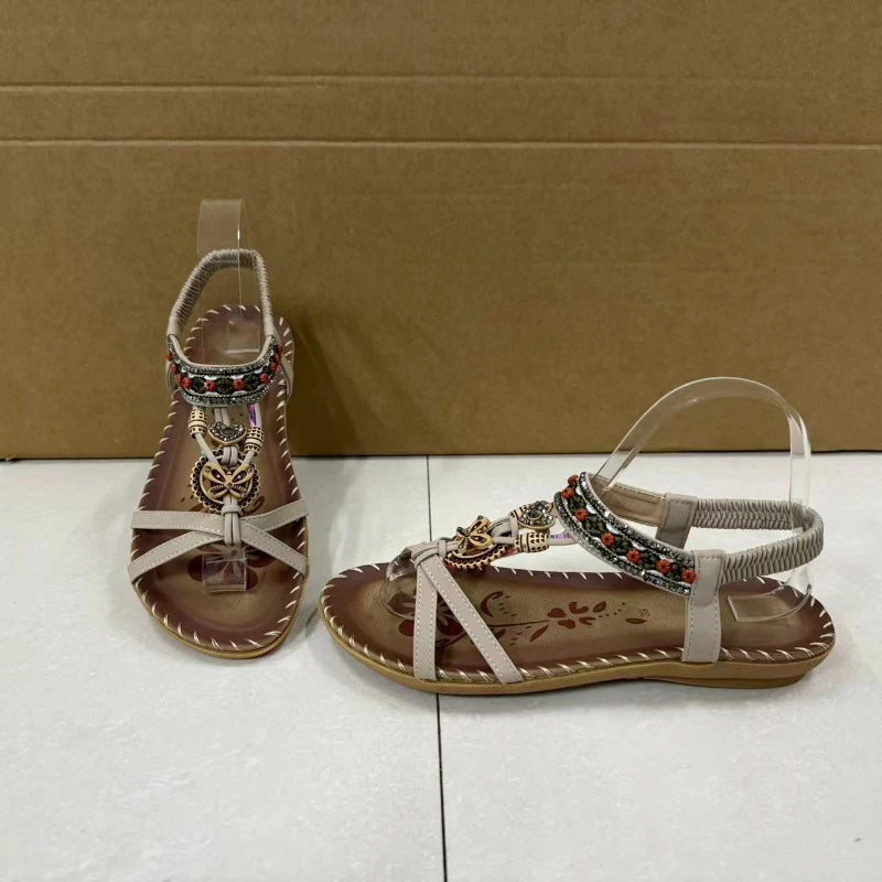 Pair of brown sandals with decorative straps on a white surface and brown cardboard background
