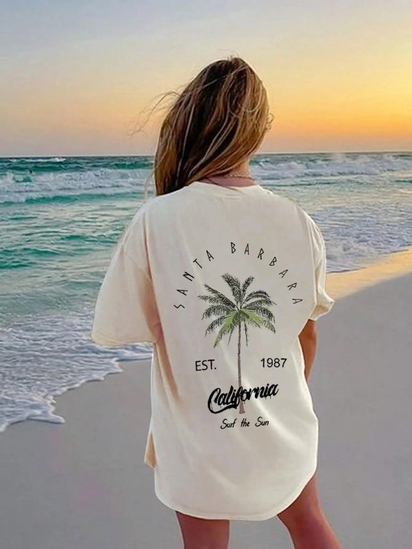 Person wearing a 'Santa Barbara, California' t-shirt with palm tree design on a beach at sunset.