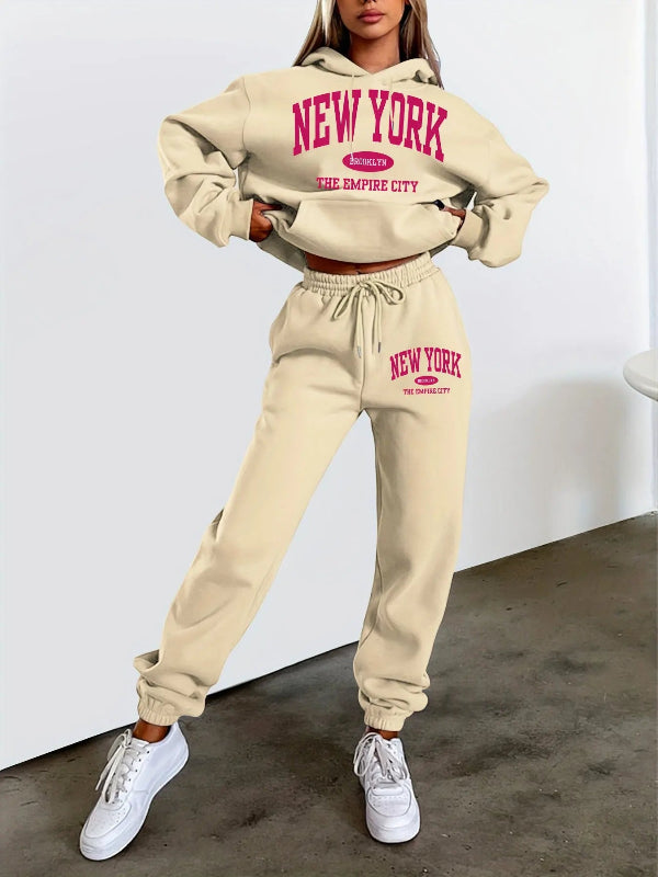 Person wearing a beige 'New York' hoodie and pants set with white sneakers on a plain background