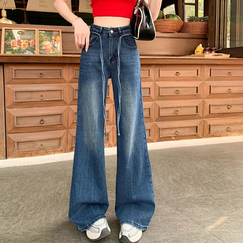 Person wearing blue flared jeans in a room with wooden furniture.
