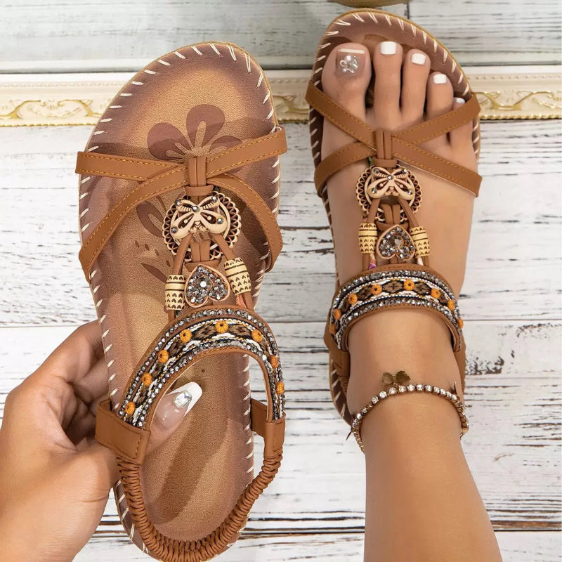 Brown sandals with decorative straps and embellishments on a wooden floor.