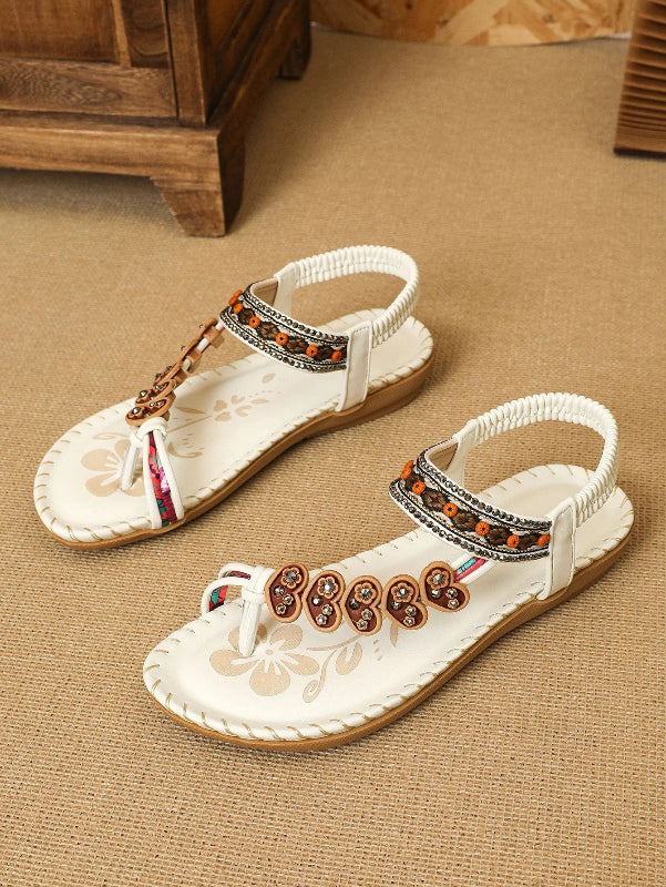 Pair of white sandals with decorative straps on a beige carpet