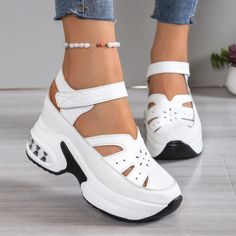 White platform sandals with black soles worn by a person on a gray floor.
