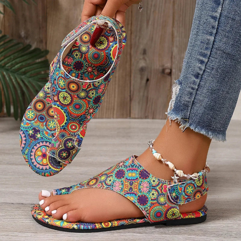 Colorful patterned sandal being worn on a wooden floor.