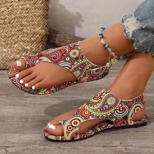 Colorful patterned sandals worn by a person on a wooden floor.