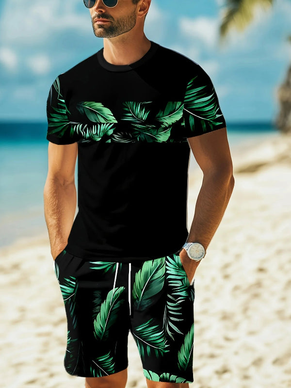 Man wearing a black t-shirt and green leaf-patterned shorts on a beach.