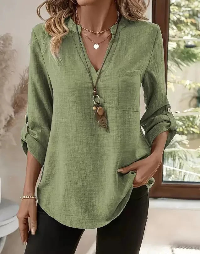 Person wearing a green shirt with a necklace, standing indoors.