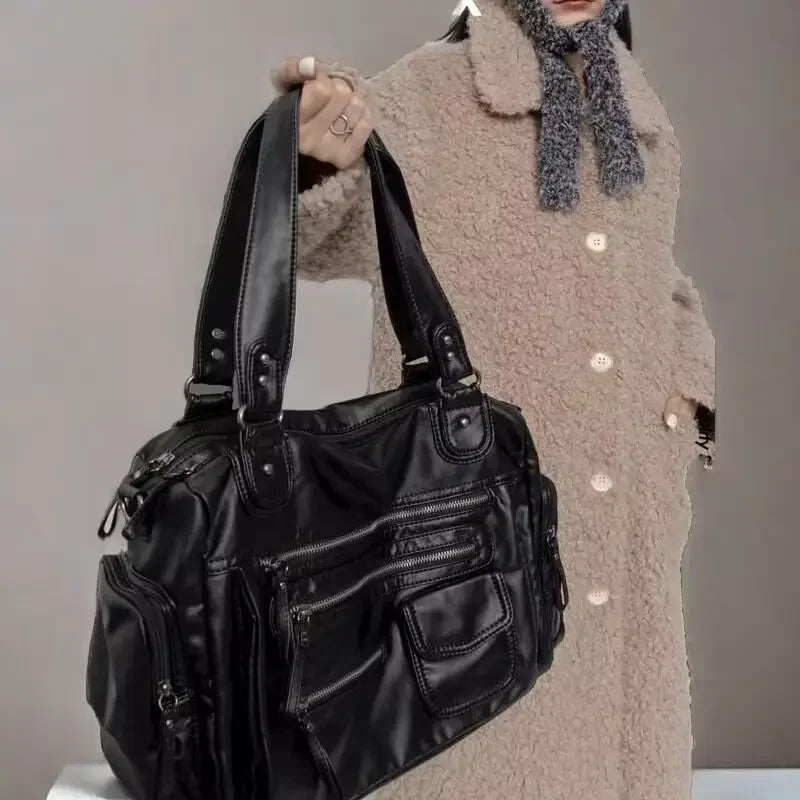 Person holding a black leather handbag against a neutral background