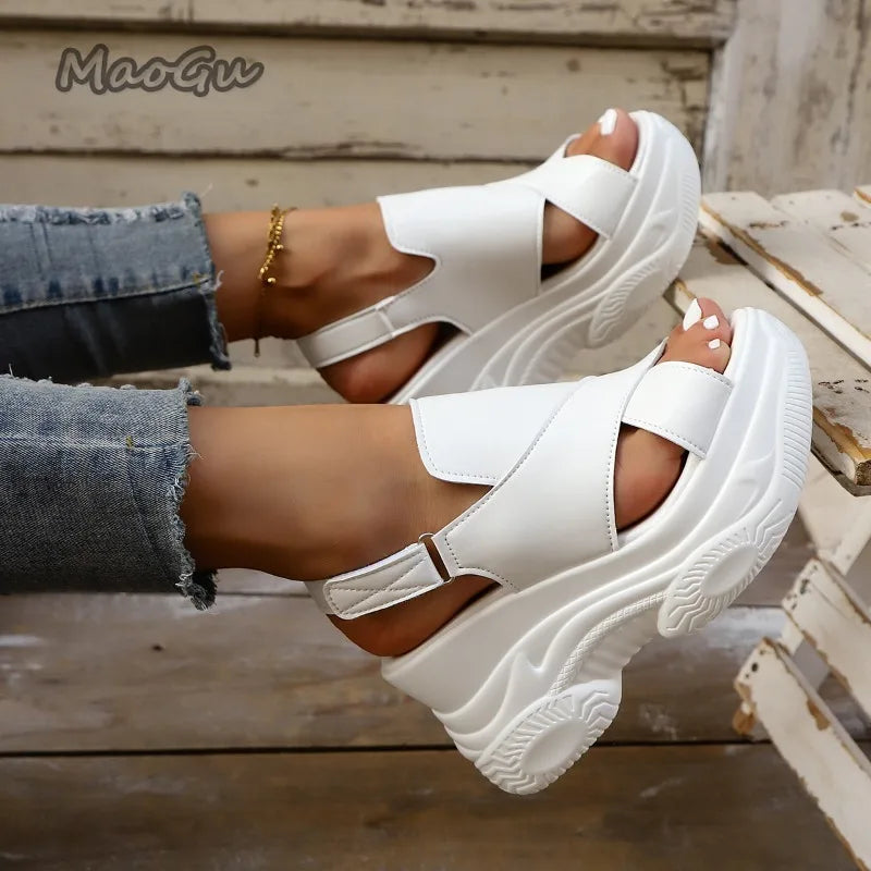 White platform sandals worn with denim jeans on a wooden floor.