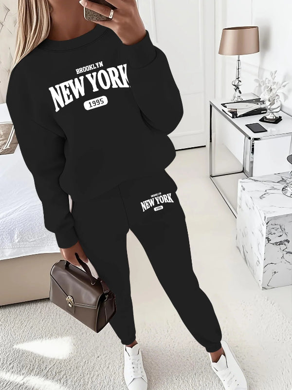 Person wearing a black 'New York' sweatshirt and pants in a room with a lamp and table.