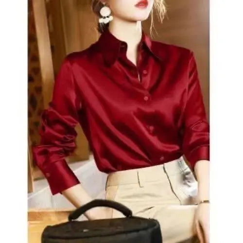 Person wearing a red satin shirt and beige pants, holding a black handbag.