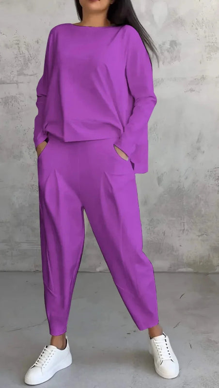 Person wearing a purple outfit with white sneakers against a gray concrete wall.